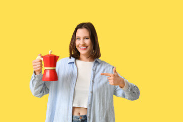 Beautiful young woman pointing at geyser coffee maker on yellow background