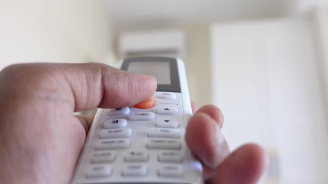 Person using air conditioner remote control to adjust home temperature and airflow settings