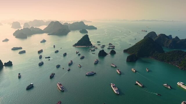 Aerial view of Halong bay limestone islands with tour cruise boats at sunset, Vietnam.