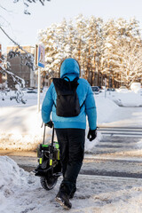 Person walking near electric unicycle monowheel crossing snowy winter street crosswalk in forest area wearing blue jacket helmet backpack showing alternative eco-friendly urban commute mobility © MarijaBazarova