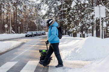 Person walking near electric unicycle monowheel crossing snowy winter street crosswalk in forest area wearing blue jacket helmet backpack showing alternative eco-friendly urban commute mobility © MarijaBazarova