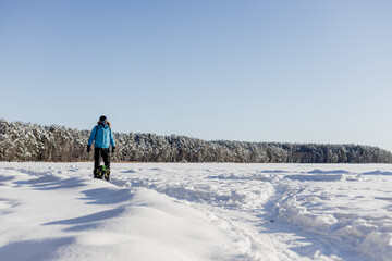 Person riding electric unicycle monowheel on frozen snow-covered lake field in winter landscape with blue sky forest background wearing safety helmet goggles, extreme outdoor adventure sport activity © MarijaBazarova