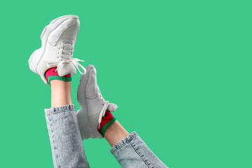 Legs of young woman in stylish white sneakers on green background