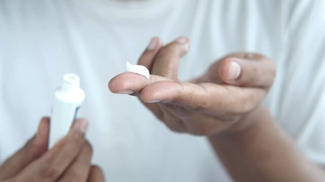 A close up view of a man holding a small white tube of toothpaste with a squeeze of white paste on his finger, highlighting dental hygiene and personal care