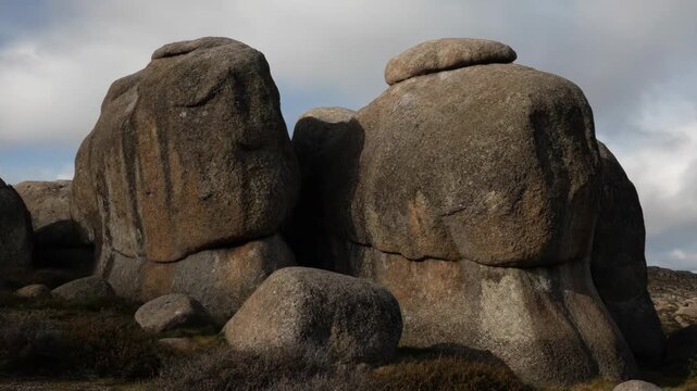 A time-lapse captures the changing light and shadows on ancient granite boulders in a wild, rocky environment.