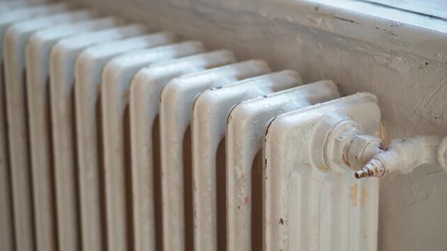 Vintage cast iron radiator under window showing old heating system details in apartment interior with daylight