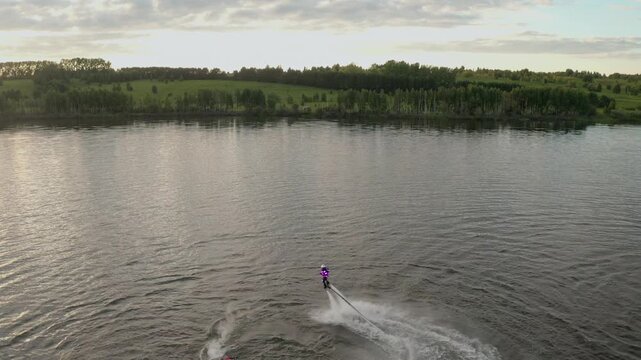 Flyboard show on open water. Athlete man performs tricks in the air over a picturesque lake. Spectacular sports. Extreme lifestyle and water activity.