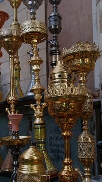 Vertical tilt-up footage of multiple ornate hookahs with engraved brass bases and decorative glass stems displayed at traditional market shop. Khan El Khalili bazaar in Cairo, Egypt