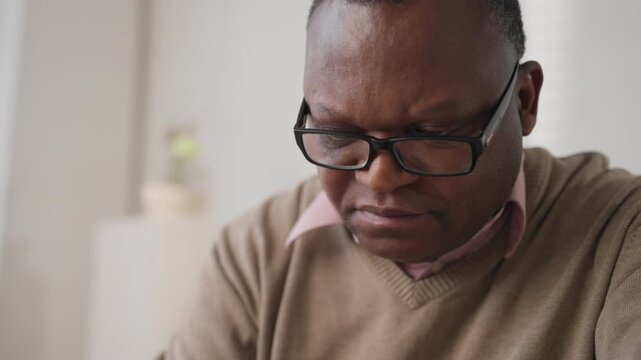 Portrait of busy african american man working at home office, closeup of face. Freelancer or businessman checking papers and sending emails, eyeglasses for vision correction, modern curing myopia