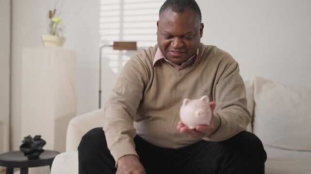 Good mood of black man saved money, african person putting coins into piggy bank . Save up money for retirement and wishes, financial literacy of modern people, economic crisis, householder save money