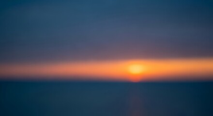 Obraz premium A blurry image of a vibrant sunset over the ocean horizon featuring a bright orange sun amidst a gradient of blue and orange hues