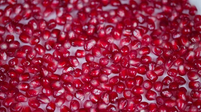 Macro shot of scattered pomegranate seeds against white background. Closeup image of radiant red pomegranate arils showcasing translucent texture and juice droplets