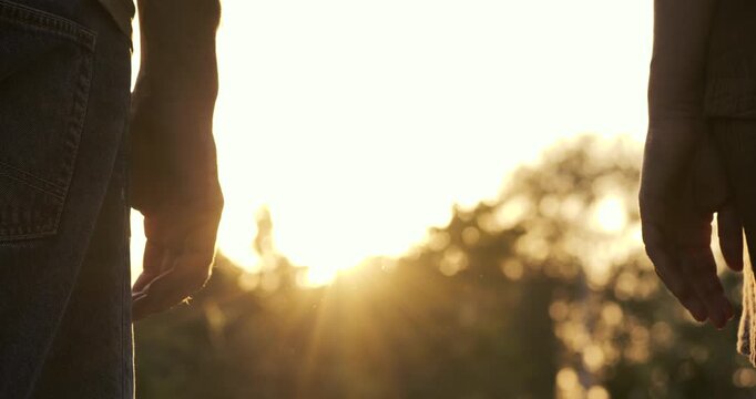 Silhouette of couple standing together at sunset. Unrecognizable man and woman enjoy golden hour outdoors. Sun flare shines between two people. Romantic scene depicts love and emotional couple bond.