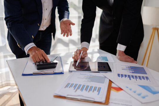 Two business people point to graphs and charts to analyze market data, balance sheet, account, net profit to plan new sales strategies to increase production capacity.
