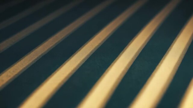 Diagonal golden light stripes are illuminating a textured surface, creating a contrasting pattern of light and shadow with repetitive lines and a rhythmic visual effect