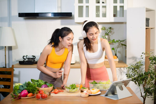 Two fit women preparing fresh salad in a modern kitchen, celebrating healthy lifestyle, fitness, clean eating, wellness, home cooking and digital recipe inspiration.