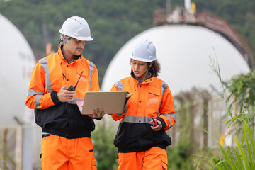 Professional technical team in hardhats discussing project maintenance outdoors at a fuel and energy plant, Industrial engineers using a laptop for technical data analysis at a gas storage facility