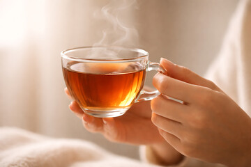 A person's hands delicately holding a steaming cup of tea, showcasing the warmth and comfort of a cozy moment. The warm light enhances the atmosphere