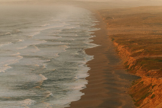 Aerial view of rugged coastline with waves at sunset