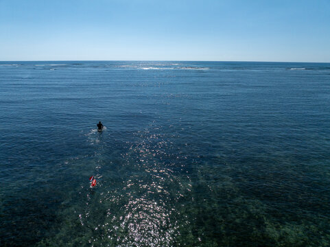 diver spearfisher walking away with red buoy shallow ocean reef