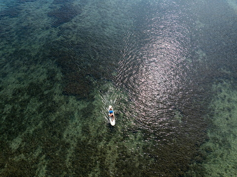 Young male surfer paddling across shallow ocean reef