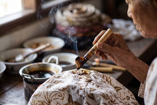 Elderly woman applying wax to fabric with traditional batik technique.