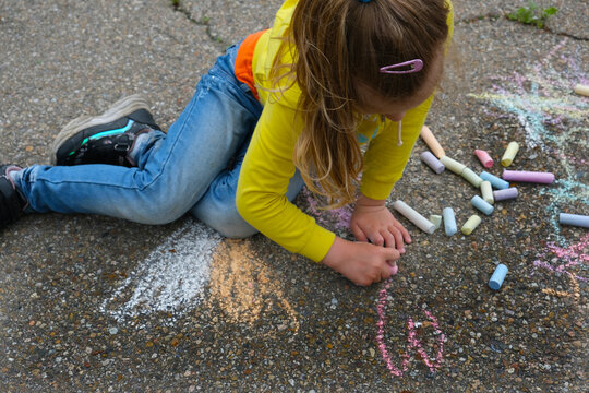 Child paints outdoors. Little girl drawing colored chalk on the asphalt . Creative development of children