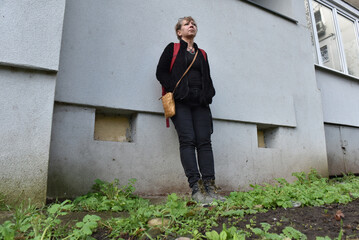 Middle-aged woman with blonde hair standing against a textured grey building wall © salajean