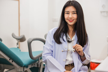 woman in a white lab coat sits in a room with a medical examination table