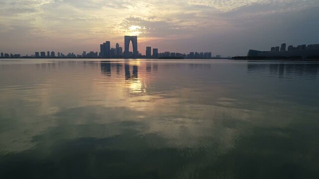 Flying backwards over beautiful calm Jinji lake with modern Suzhou skyscrapers and towers at sunset, China
