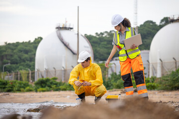 Technical team performing ecological impact assessment and water quality analysis at a coastal industrial zone with gas tanks, Industrial safety inspectors conducting environmental research