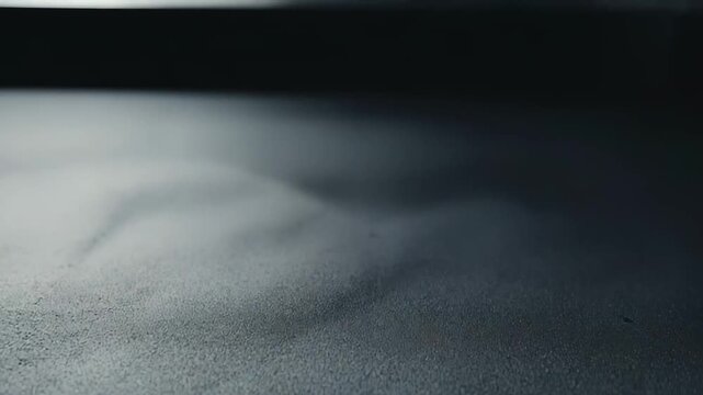 Water droplets accumulating on a dark, textured surface, creating a delicate pattern of condensation and moisture, with a soft, out of focus background