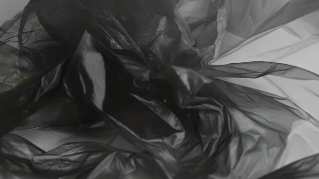 Crumpled black plastic film creating a dark abstract background with translucent textures and random golden light particles floating throughout the space