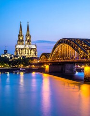 Cityscape showing a cathedral and bridge illuminated at night over water with sky