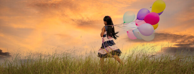Banner Cheerful cute girl holding balloons run green meadow violet purple pastel sky happiness. Banner Hands holding vibrant air balloons birthday party happy times summer pueple sky with copy space