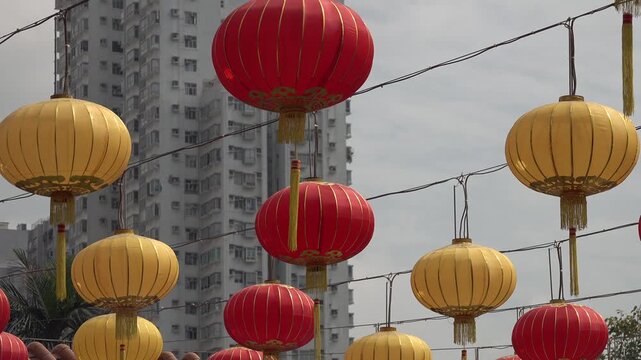 Classic red and yellow Chinese lanterns at famous Wong Tai Sin temple contrast with modern residential apartment building in Hong Kong

