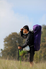 Hiker with large purple backpack shielding eyes to survey distant landscape