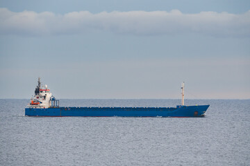 Fototapeta premium Large blue industrial cargo ship transporting goods across the calm open sea under a cloudy sky during a commercial maritime voyage
