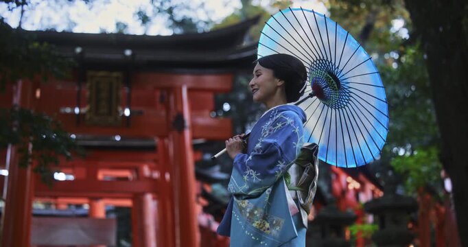 Beautiful, smiling, happy Japanese woman in kimono holding umbrella near torii gates