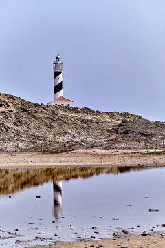 Menorca lighthouse reflection on a peaceful day, a landmark on the rugged Balearic Islands coast