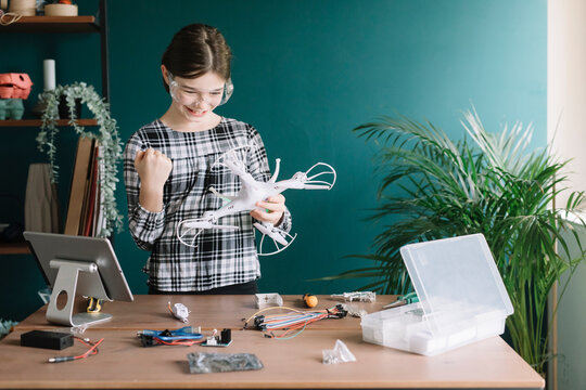 Smiling girl holding drone gesturing while standing against wall at home