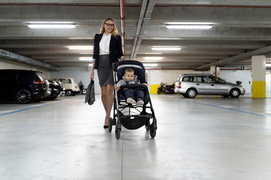 Young businesswoman pushing stroller with baby boy in car park