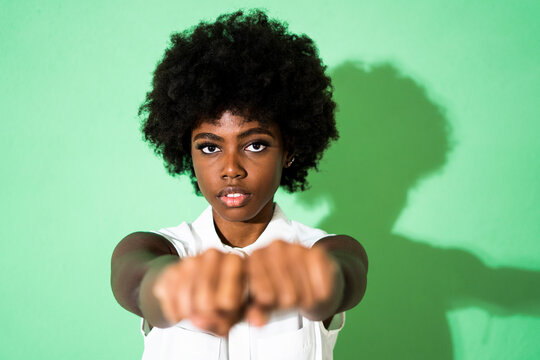 Young woman showing fist while standing against green background