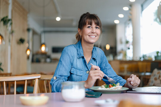 Female owner eating food while sitting in cafe