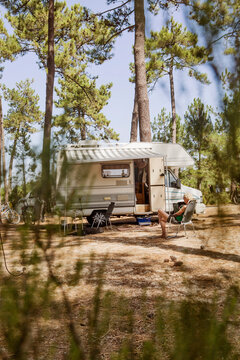 France, Gironde, woman sitting in front of camper on a camping ground using digital tablet