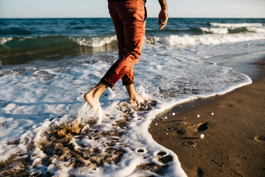 Rear view of man with orange trousers walking on a beach at water's edge
