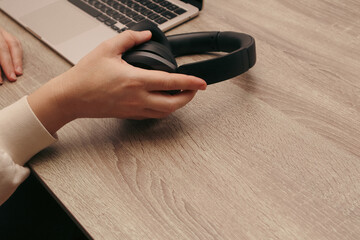 Woman's hand picking up black wireless headphones from a wooden office desk.