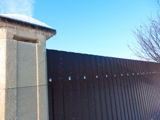 Brown metal fence and stone pillar covered in ice under a clear blue sky.