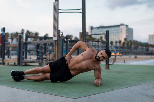 Barechested muscular man doing side planks outdoors