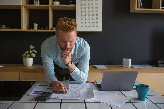 Man with laptop studying plans on table at home
